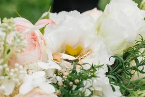 Golden wedding rings and a beautiful wedding bouquet of roses and eustoma in the background close-up. Details and wedding traditions. photo