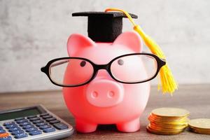 Pigging bank wearing eyeglass with coins and calculator saving bank education concept. photo