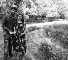 Indian couple posing for maternity baby shoot. The couple is posing in a lawn with green grass and the woman is falunting her baby bump in Lodhi Garden in New Delhi, India - Black and White photo