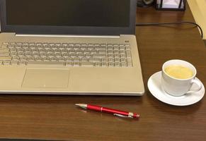 cómodo lugar de trabajo en la oficina con mesa de madera, portátil, bolígrafo y taza de café. foto