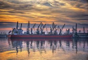 Ship and cranes in port at sunset. Cargo ship terminal at twilight scene. photo