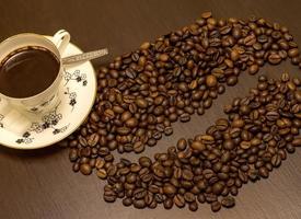 A cup of coffee and coffee beans like one big bean on the table. photo