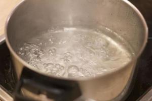 agua hirviendo en una sartén sobre una estufa eléctrica en la cocina con humo. cerca foto