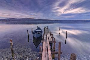 emocionante paisaje de larga exposición en un lago con muelle de madera y barco. foto