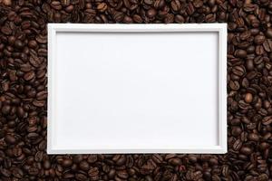 Roasted coffee beans surround a frame on a white background. Copy space. Top view. photo