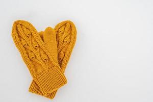 Knitted yellow mittens lie on pure white snow on a cloudy winter day. Copy space. Top view. photo