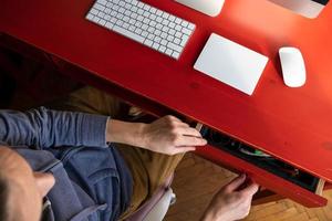 Woman opens a desktop drawer and wants to take something from there, on which there is a keyboard, touchpad and a computer. photo