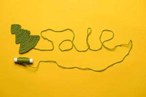 Sale made of green threads going from a knitted Christmas tree to a spool, on a yellow background. Concept of New Years discounts. photo