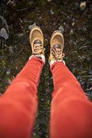 Female feet in yellow suede boots stand in moss with stones. Top view. Vertical photo. photo