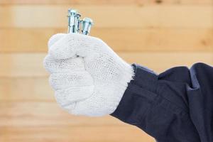 Hand in glove holding metal anchor bolts photo