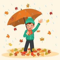 niño feliz sosteniendo paraguas bajo la lluvia con hojas caídas en otoño vector