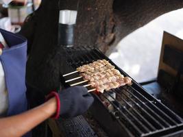 Hand holding grilled pork sticks on fire flaming in steel stove vintage style, delicious Thai street food and popular concept  . photo