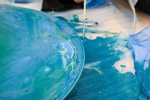 The process of creating a home-made trendy abstract modern pattern painted with a brush of acrylic blue multi-colored resin on a round wooden board photo