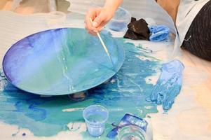 The process of creating a home-made trendy abstract modern pattern painted with a brush of acrylic blue multi-colored resin on a round wooden board photo
