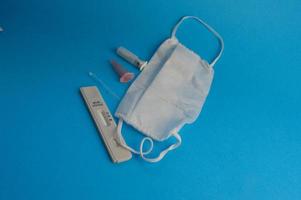 antibody test. a strip for self-diagnosis for coronavirus infection on a blue background. next to the test, a disposable mask, a lancet and a pipette for taking an analysis with a container for blood photo