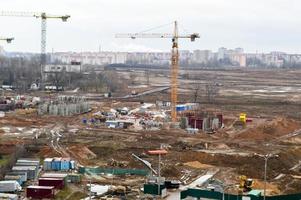 vista superior del sitio de construcción durante la construcción de una nueva urbanización con casas altas, nuevos edificios con la ayuda de grandes grúas industriales y equipo profesional en una gran ciudad foto