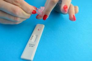 test strip for the determination of coronavirus on a blue background. lab with red manicure dripping solution to detect antibodies. fingerstick sampling for coronavirus detection photo