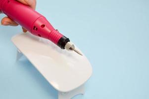 The process of making a beautiful manicure on the hands on the fingers with the help of a special machine and a lamp for drying the varnish in the nail beauty salon on a blue background photo