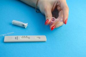 a pink plastic container for blood collection. a girl with a red manicure holds a small form for taking blood in her hands. self-diagnosis of the virus. home test for coronavirus photo