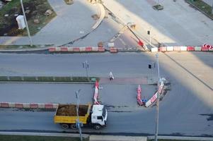 A large dump truck rides to a construction site and carries sand along an asphalt road. View from above photo