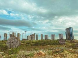 construction of multi-storey buildings in the city center. tall houses made of concrete blocks and slabs. bulky cranes are building houses, against the backdrop of a field photo