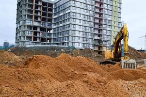 Big bright yellow powerful industrial heavy excavator tractor, bulldozer, specialized construction equipment for road repair during the construction of a new micro-district in a big city photo