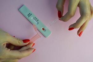 coronavirus test on a pink matte background. medical procedure. girl with bright red nails doing an analysis for IgG and IgM antibodies. a drop of blood added to the strip photo