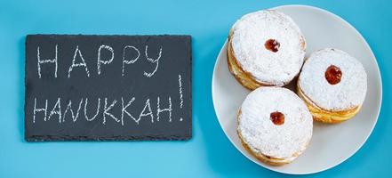 Happy Hanukkah. Jewish dessert sufganiyot donuts on blue background. Symbol of religious Judaism holiday. Inscription on chalk board. photo