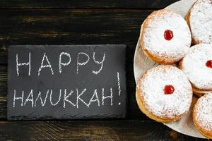 Happy Hanukkah. Traditional dessert Sufganiyot on dark wooden background. Donuts, candles and gifts. Celebrating Jewish holiday. photo