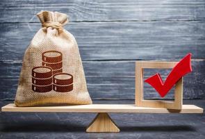 Red vote tick and a money bag on scales. The concept of lobbying for decisions and laws. Corruption risks. Estimating cost of making a decision and consequences in the future. Economic preferences photo