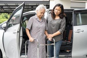 Help and support asian senior or elderly old lady woman patient walk with walker prepare get to her car, healthy strong medical concept. photo