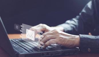Businessman hands using Laptop typing on keyboard and surfing the internet on office table with email icon, email marketing concept, send e-mail or newsletter, online working internet network. photo