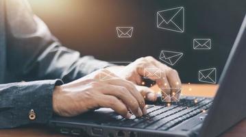 Businessman hands using Laptop typing on keyboard and surfing the internet on office table with email icon, email marketing concept, send e-mail or newsletter, online working internet network. photo