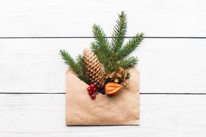 Christmas tree branch cone flowers decoration in paper envelope on white wooden background photo