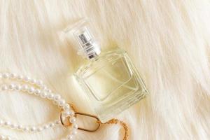 a transparent bottle of cosmetic products lies on beige fur with a long pile and pearl decoration. the concept of perfumery and beauty. photo