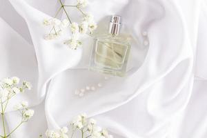 una botella de perfume de mujer o de agua de tocador yace en los pliegues de tela de raso blanco con una delicada gypsophila. el concepto de perfumería y belleza. foto