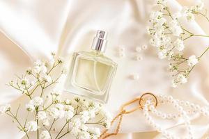 vista superior de una botella de perfume de mujer sobre un fondo pastel de tela satinada con un collar de perlas y gypsophila. publicidad de la fragancia. foto