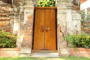 puerta de madera pintada de color marrón claro entre la pared de ladrillos rotos.la puerta está cerrada pero desbloqueada.