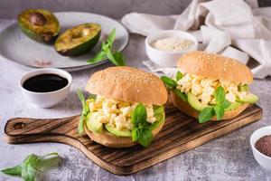 Hamburger with avocado, scrambled eggs and basil on a board on the table. Healthy food. photo