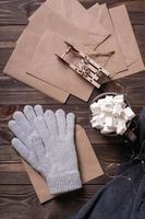 Winter still life. Drink with marshmallow, wool gloves and craft envelopes on a wooden background. photo