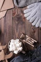 Winter still life. Drink with marshmallow, sled, woolen socks and gloves on a wooden background. photo
