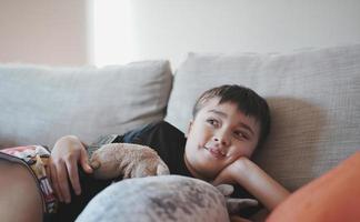 Indoor portrait kid looking up with smiling face, Happy boy lying on sofa watchig TV or relaxing in morning, Comfortable Child laying down on couch,Positive children concept photo