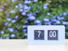 reloj blanco que muestra las 7.00 en la mesa en el jardín con fondo de flores violetas. foto