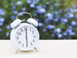 white vintage alarm clock and cup of coffee on the table in the garden with purple flowers background. photo