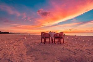 Table setup for wedding ceremony on sunset beach. Romantic destination dining, couple anniversary romance celebration. Love arrangement togetherness dinner on island shore. Amazing sky sea view photo