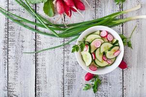 Fresh salad of cucumbers and radishes in a white bowl on the old wooden background photo