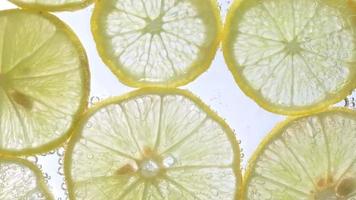 Juicy lemon slices with bubbles under water isolated on white background. Yellow lime slices pattern textured background. video