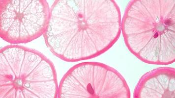 jugosas rodajas de limón con burbujas bajo el agua aisladas en fondo blanco. fondo de textura de patrón de rodajas de lima rosa. video