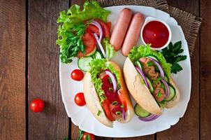 Hot Dog con salsa de tomate, mostaza, lechuga y verduras en la mesa de madera foto