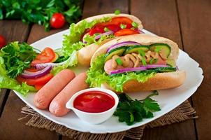 Hot Dog con salsa de tomate, mostaza, lechuga y verduras en la mesa de madera foto